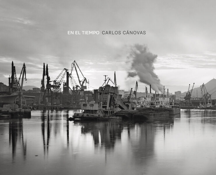 en la portada del catálogo de la exposición de Carlos Cánovas se ve un puerto con barcos de carga, es una obra del autor en blanco y negro de gran belleza.
