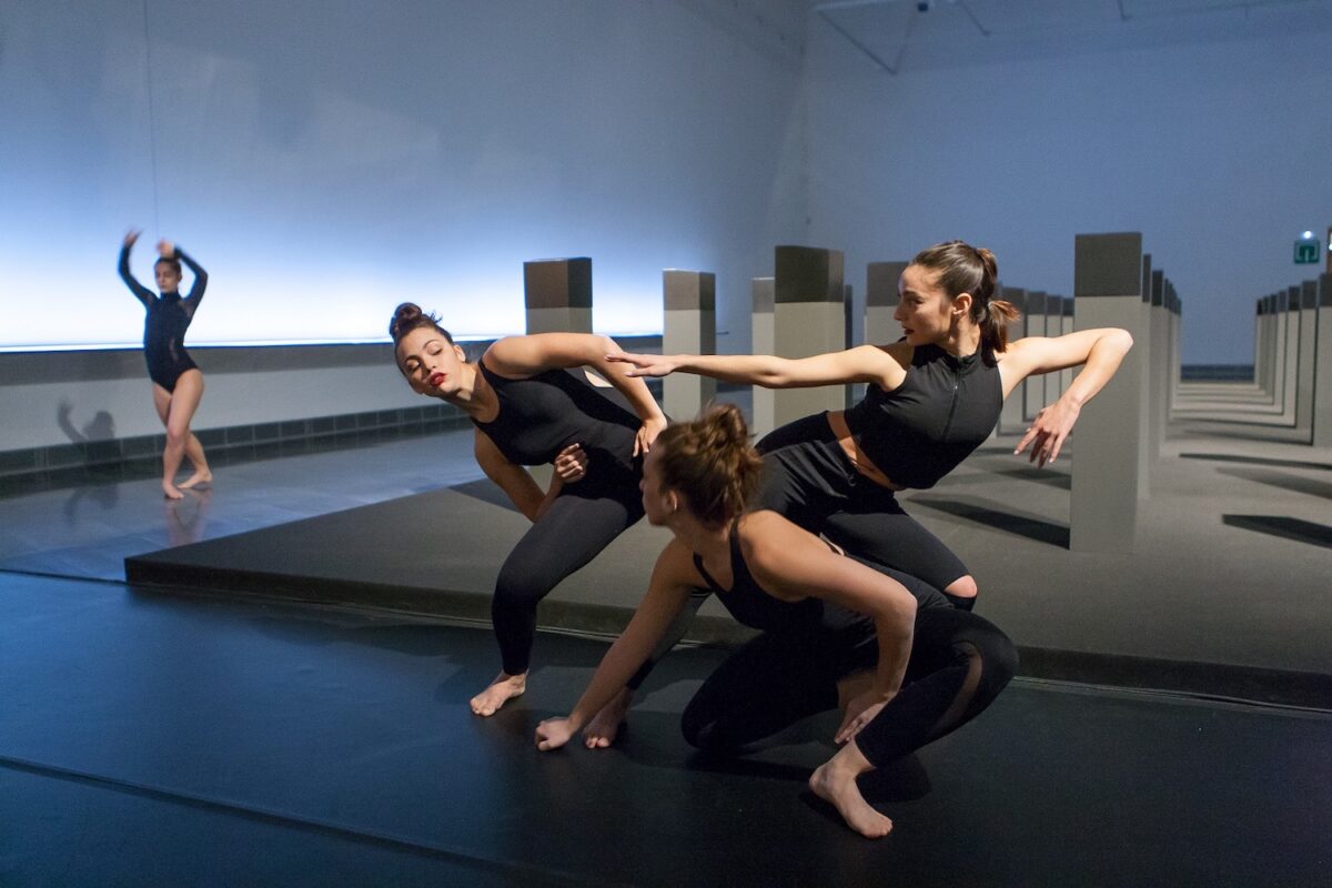 En la imagen varias bailarinas vestidas de negro evolucionan en una pieza que se danzó en las salas del Museo ante la obra Menhires de la exposición de Elena Assins. 