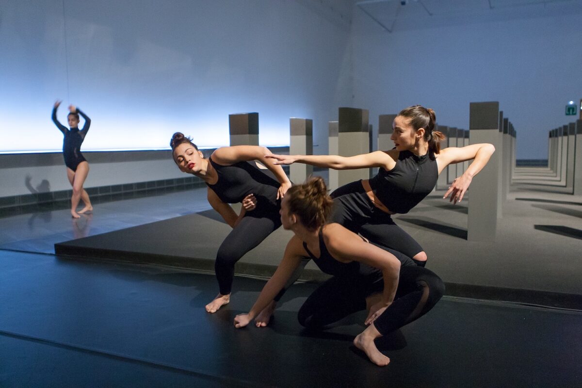 En la imagen varias bailarinas vestidas de negro evolucionan en una pieza que se danzó en las salas del Museo ante la obra Menhires de la exposición de Elena Assins. 