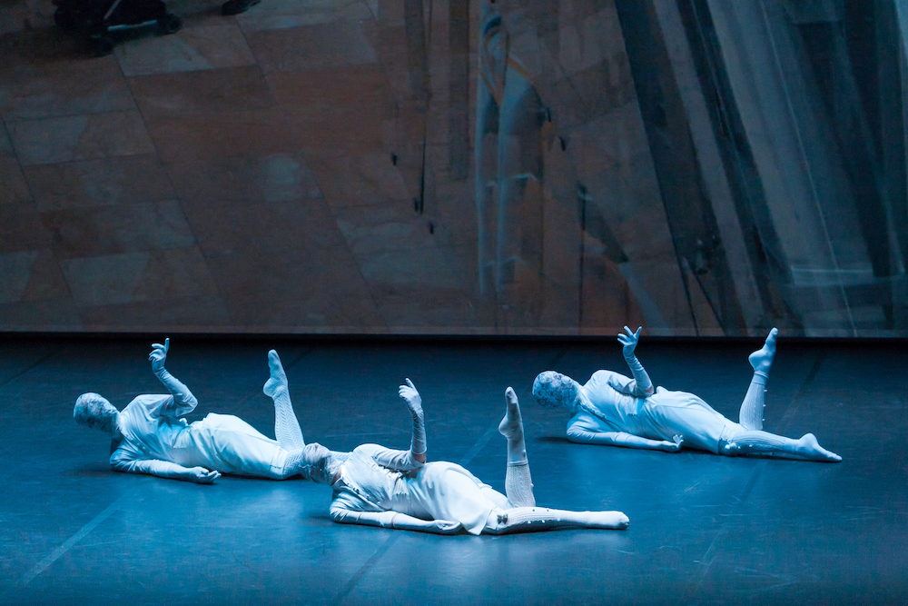 La producción Oskara de Kukai Dantza es un trabajo de reflexión sobre nuestras raices, la danza, la tradición, y las preguntas del ser humano, la comunicación. en la imagen una escena de esa coreografía, los bailarines bailan desde el suelo vestidos de blanco del pie a la cabeza que llevan cubierta por una tela de encaje como en la danza tradicional vasca.